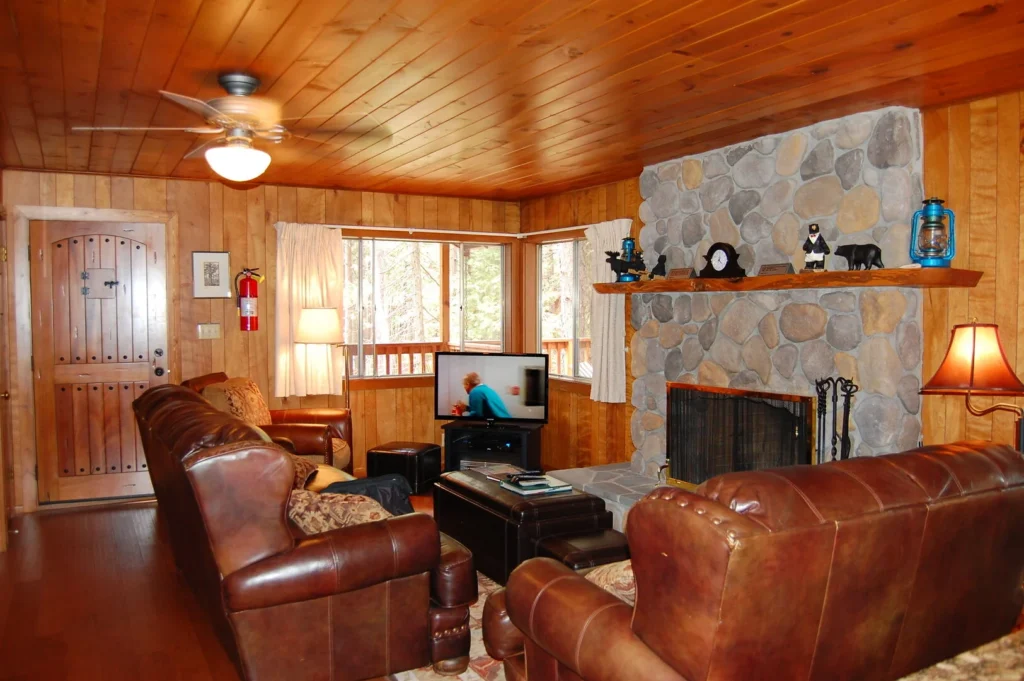 living room with wood paneling and stone fireplace, leather couches and chairs