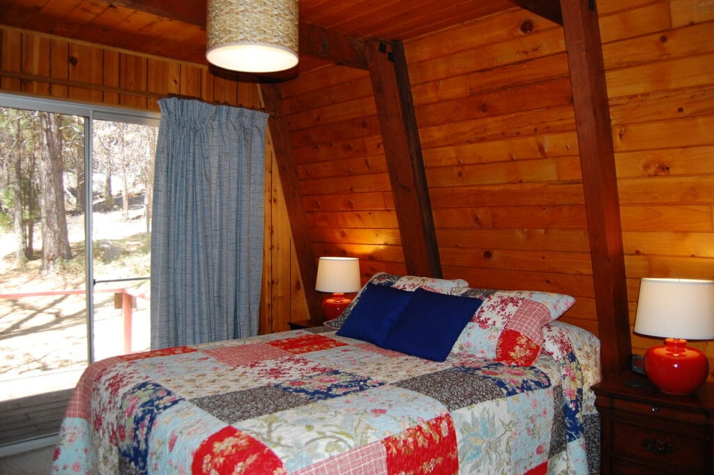 bedroom with wood walls and beams. with sliding doors to deck