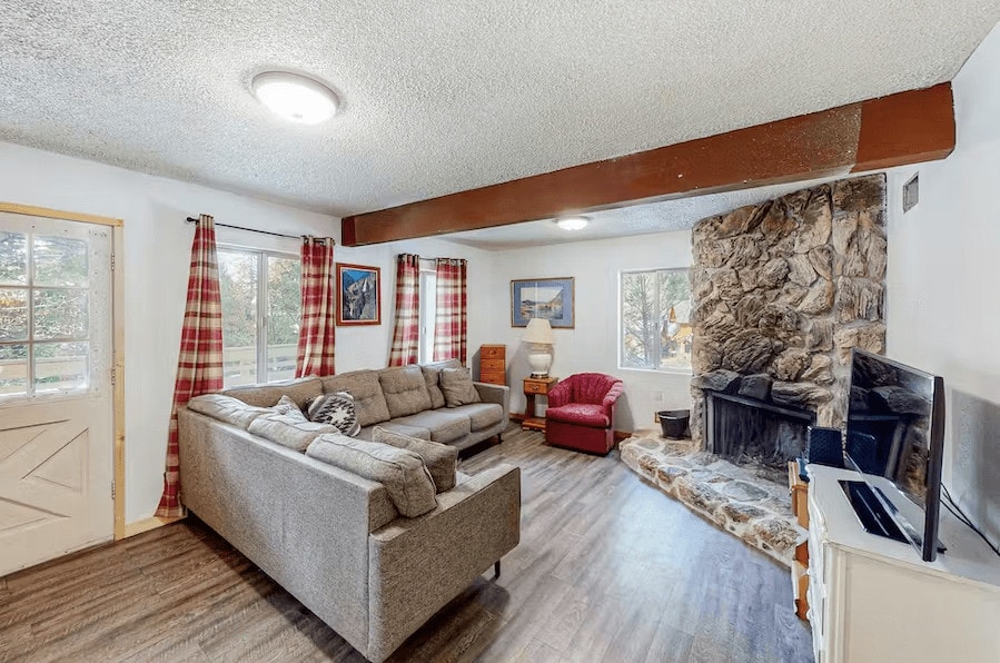 living room with beams, couches, and a stone fireplace