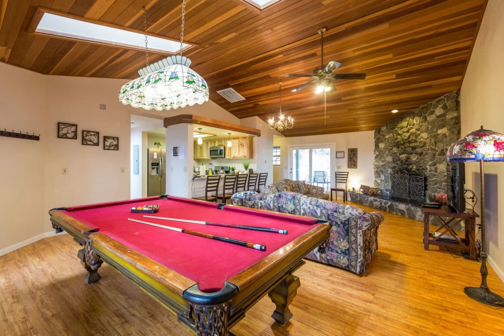 living room with stone fireplace, wood ceiling, and pool table