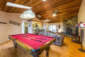 living room with stone fireplace, wood ceiling, and pool table