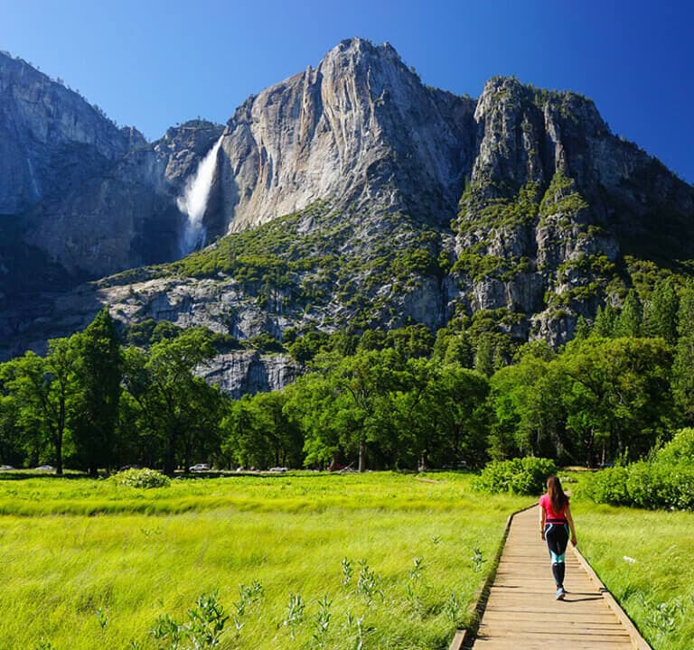 Woman walking on a boardwalk with a view of Yosemite Falls