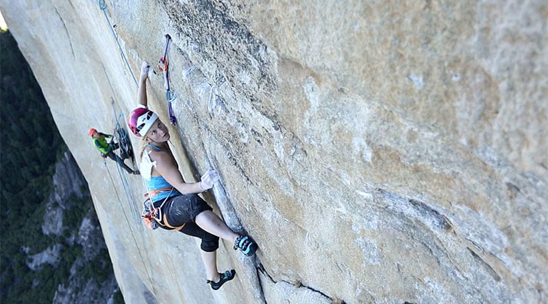 Emily Harrington free climbing Golden Gate (5.13 VI, 41 pitches) on El Capitan. Notice the belayer behind her managing the ropes she uses for protection and the gear near her left hand.