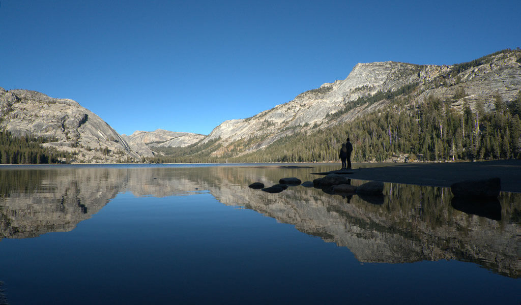 A couple stands on a rocky shore of Tenaya Lake