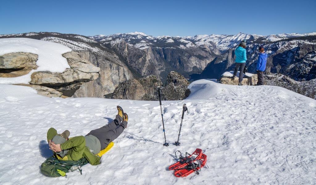 People relaxing and enjoying the snowy views from Dewey Point in Yosemite in winter.
