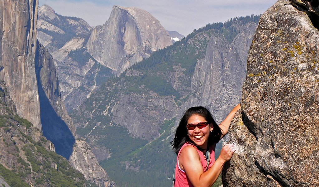Woman climbing boulder with view of Half Dome