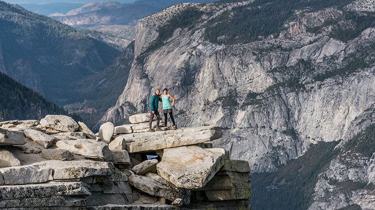 Two hikers posing for summit photos on the top of Half Dome while enjoying views of Yosemite National Park