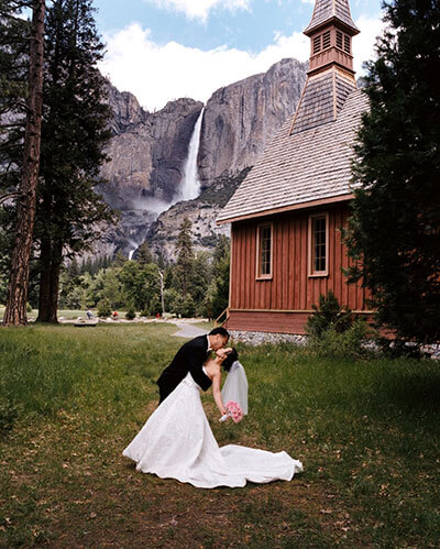 Wedding kiss by the Yosemite Valley Chapel with Yosemite Falls in the background.