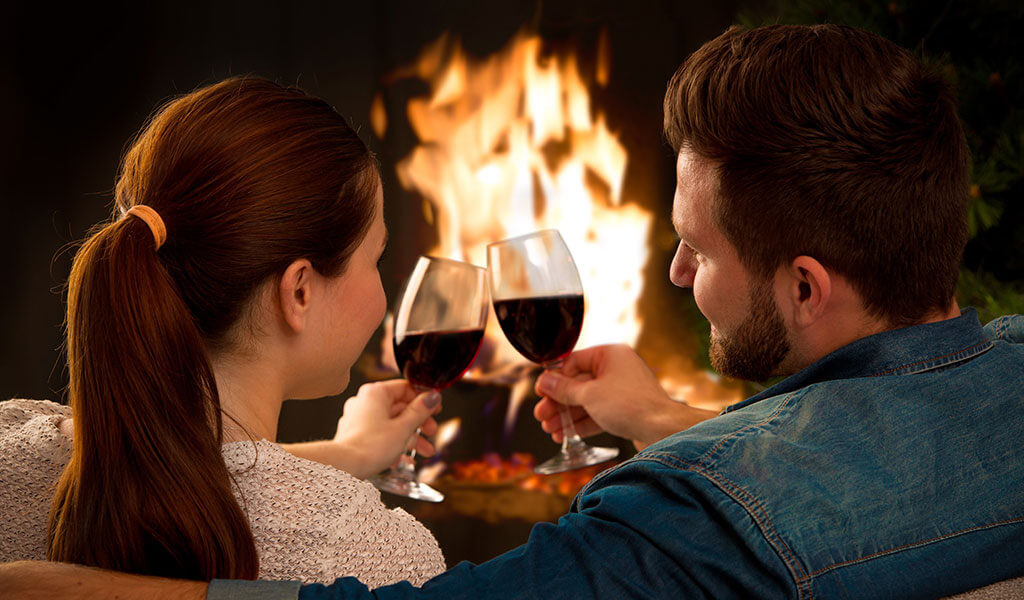 Couple toasting in front of a cozy fireplace.