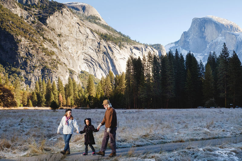 Grandparents walking with their grandchild with Half Dome in the background.
