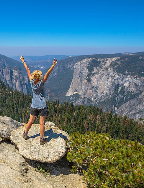 woman with hands raised on sentinel dome overlooking yosemite valley