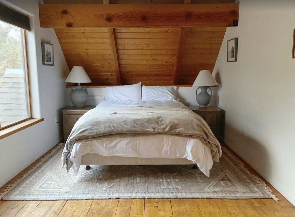 bedroom with window, sloped wood ceiling and two lamps