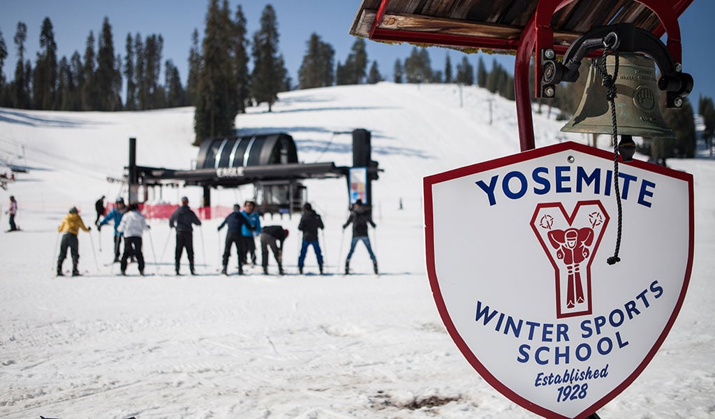 The sign for the Badger Pass ski school with instructors giving lessons in the background