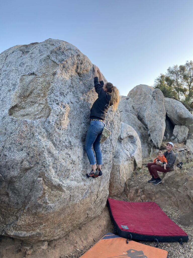 woman climbing boulder while man and baby watch